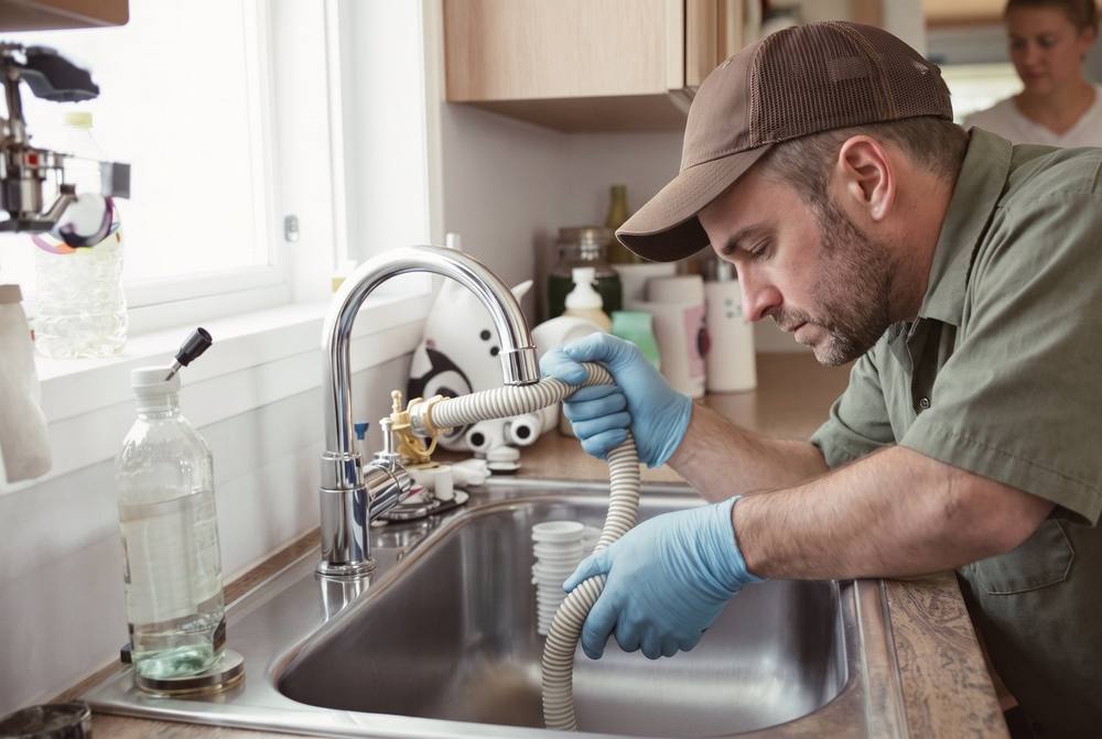 Licensed plumber repairing a water heater connection in a Kansas City rental duplex